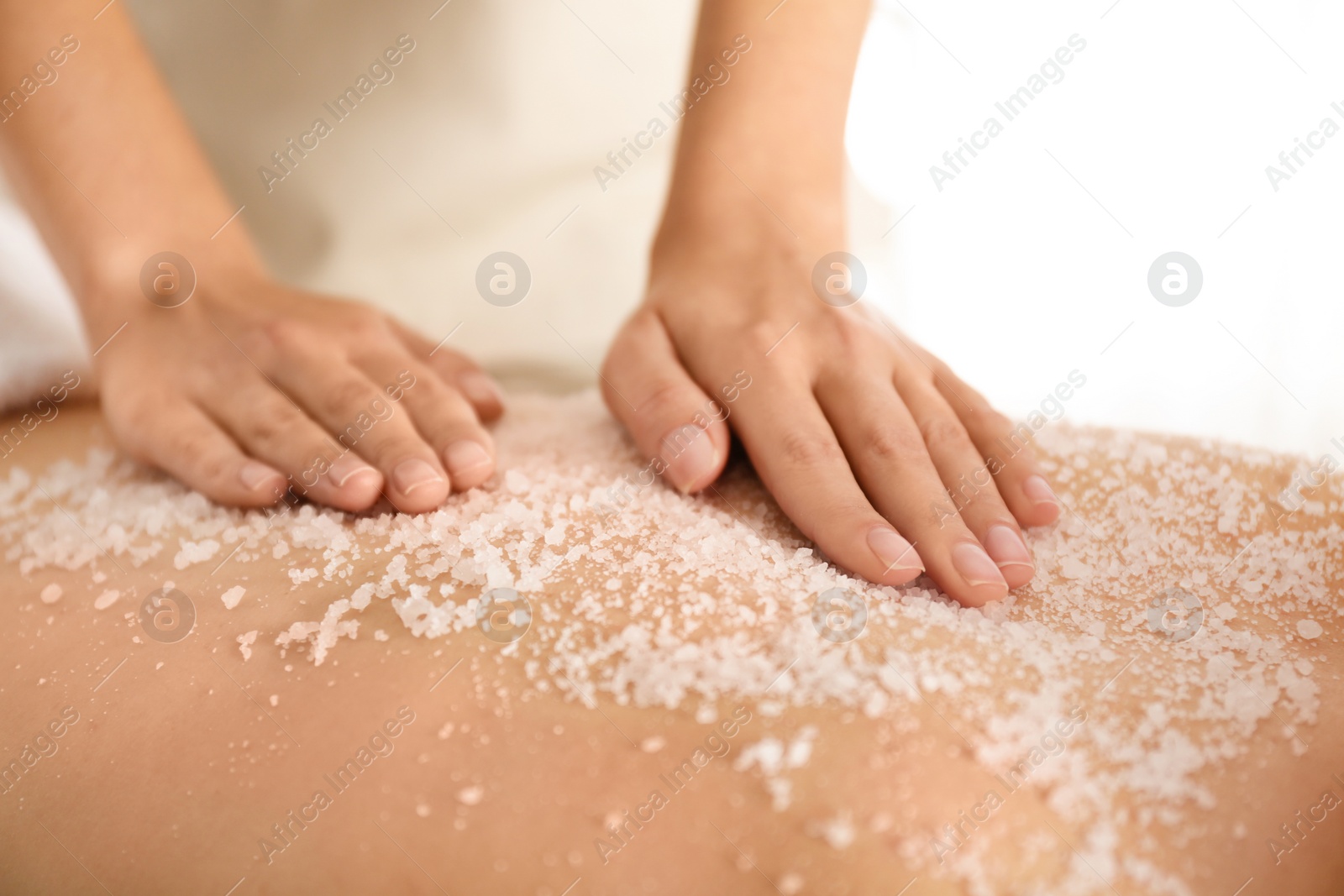 Photo of Young woman having body scrubbing procedure with sea salt in spa salon, closeup