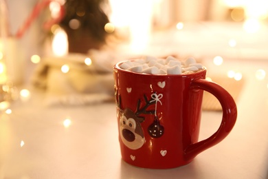 Hot drink with marshmallow and festive lights on table indoors