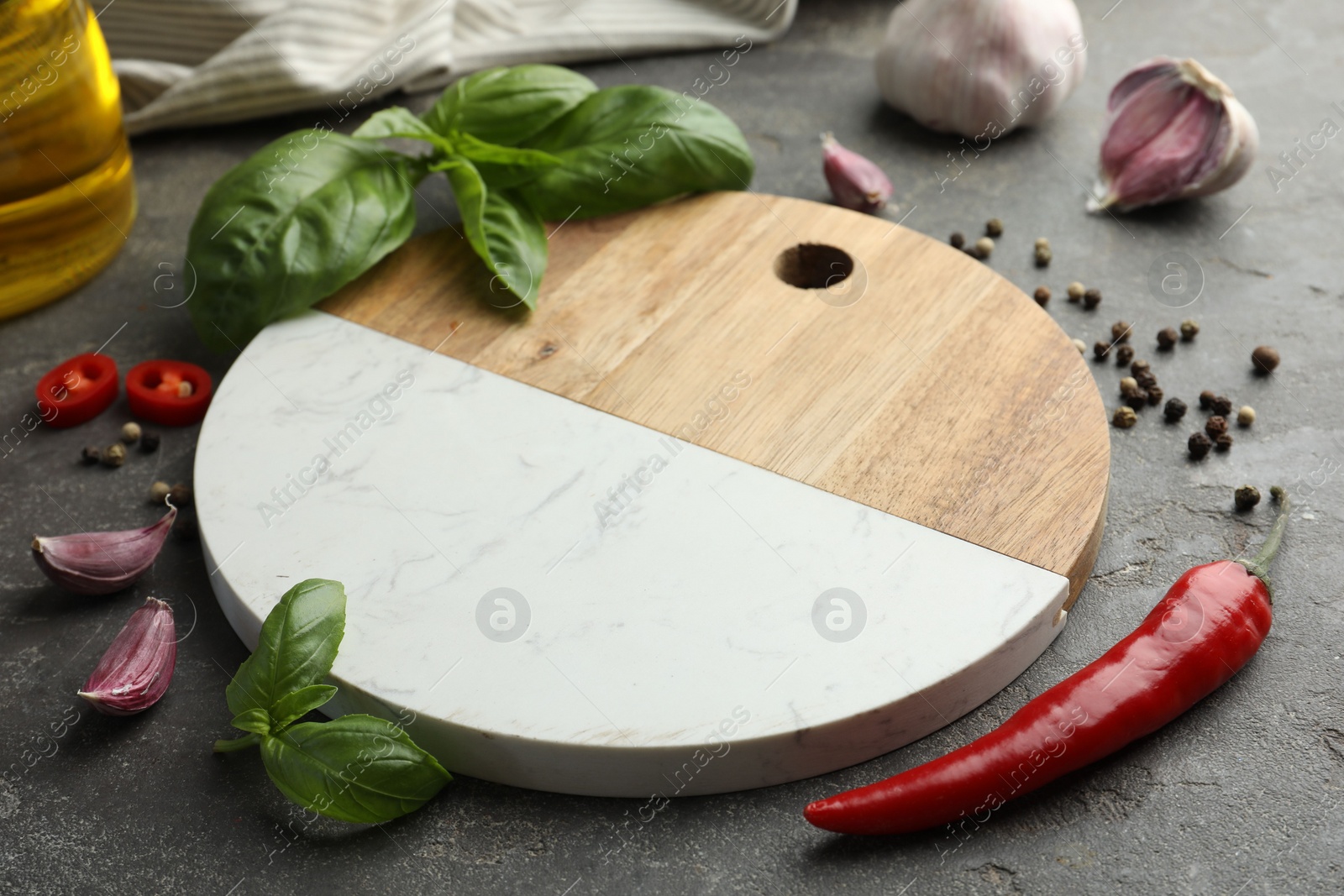 Photo of Cutting board, basil, pepper, chili peppers and garlic on grey table. Space for text