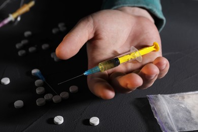 Photo of Addicted man with syringe near drugs at black textured table, closeup