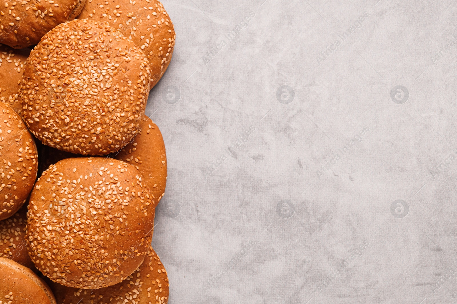 Photo of Fresh buns with sesame seeds on light grey table, flat lay. Space for text