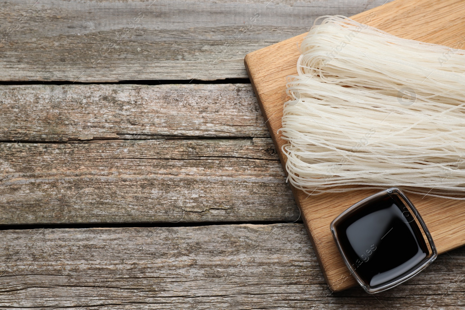 Photo of Dried rice noodles with soy sauce on wooden table, top view. Space for text