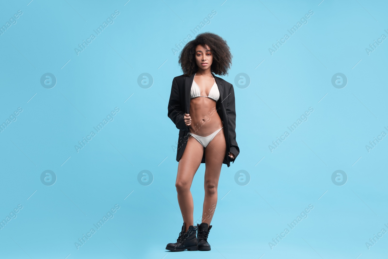 Photo of Beautiful woman in stylish bikini and jacket on light blue background