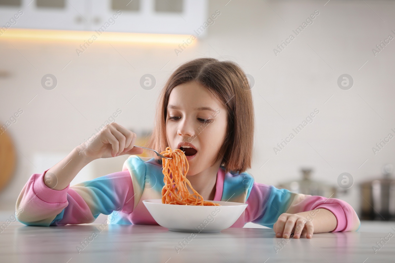 Photo of Girl eating tasty pasta at table in kitchen