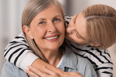 Daughter kissing her mature mother on cheek indoors