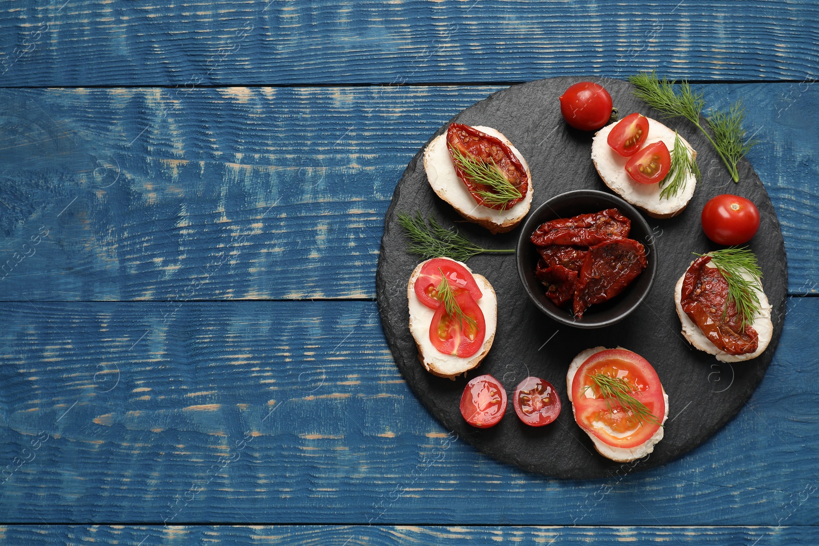 Photo of Delicious bruschettas with ricotta cheese, tomatoes, and dill on blue wooden table, top view. Space for text