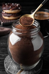 Photo of Spoon of instant coffee over jar on black wooden table