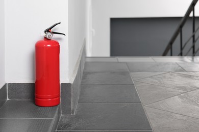 Red fire extinguisher near white wall, space for text