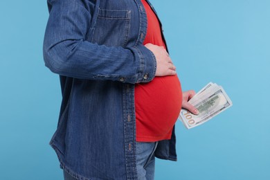 Surrogate mother. Pregnant woman with dollar banknotes on light blue background, closeup