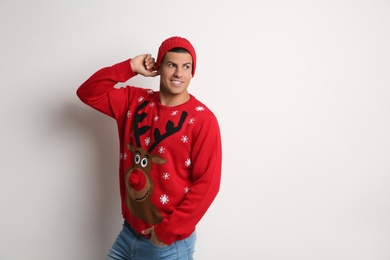 Handsome man in Christmas sweater and hat on white background, space for text