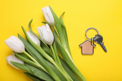 Beautiful spring flowers and key with trinket in shape of house on yellow background, flat lay