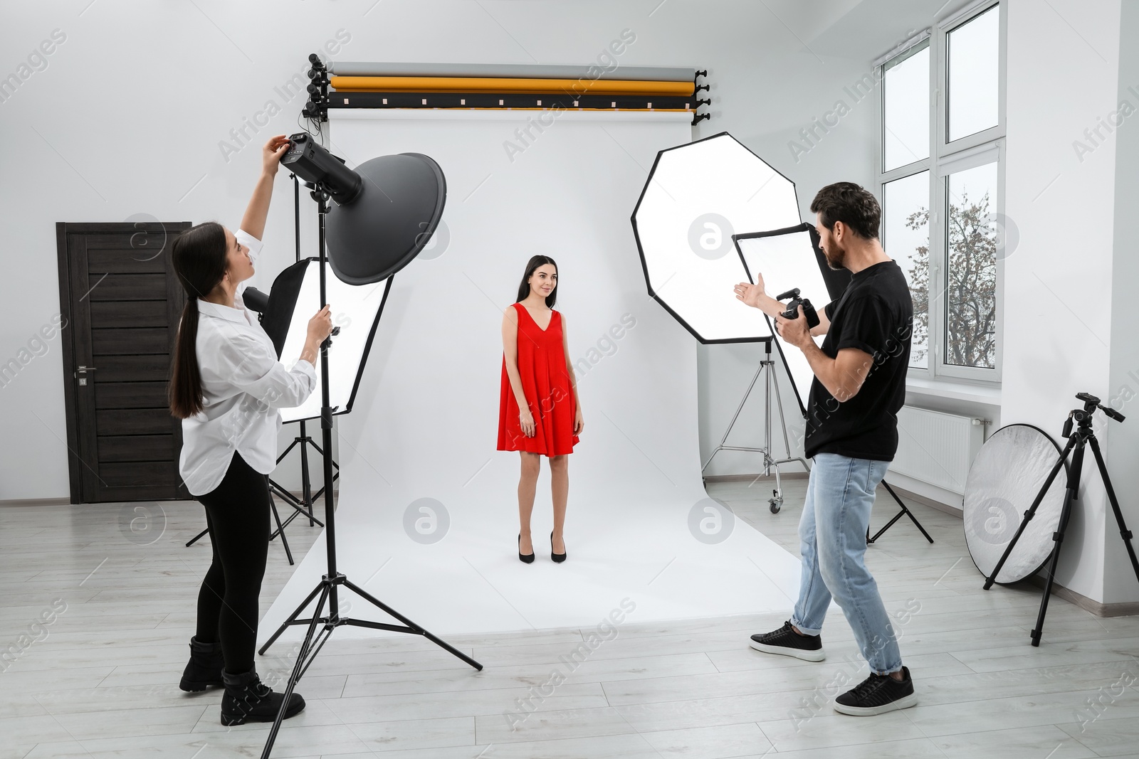 Photo of Professional photographer and assistant working with beautiful model in modern photo studio