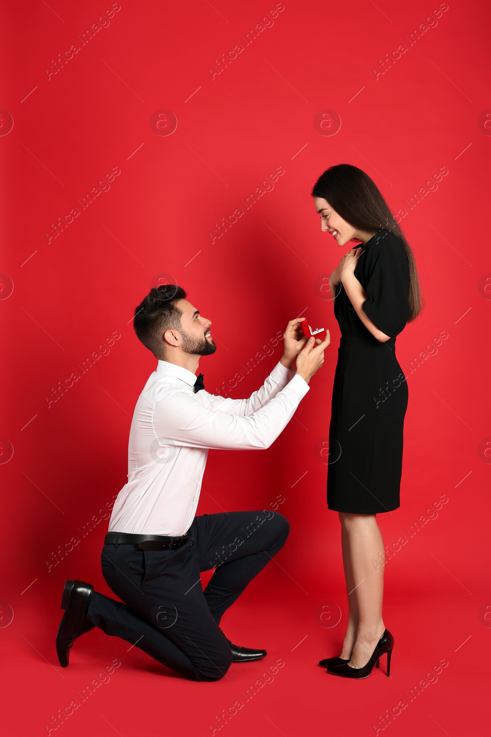 Photo of Man with engagement ring making marriage proposal to girlfriend on red background