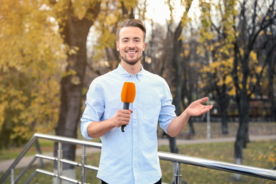 Image of Young male journalist with microphone working in park