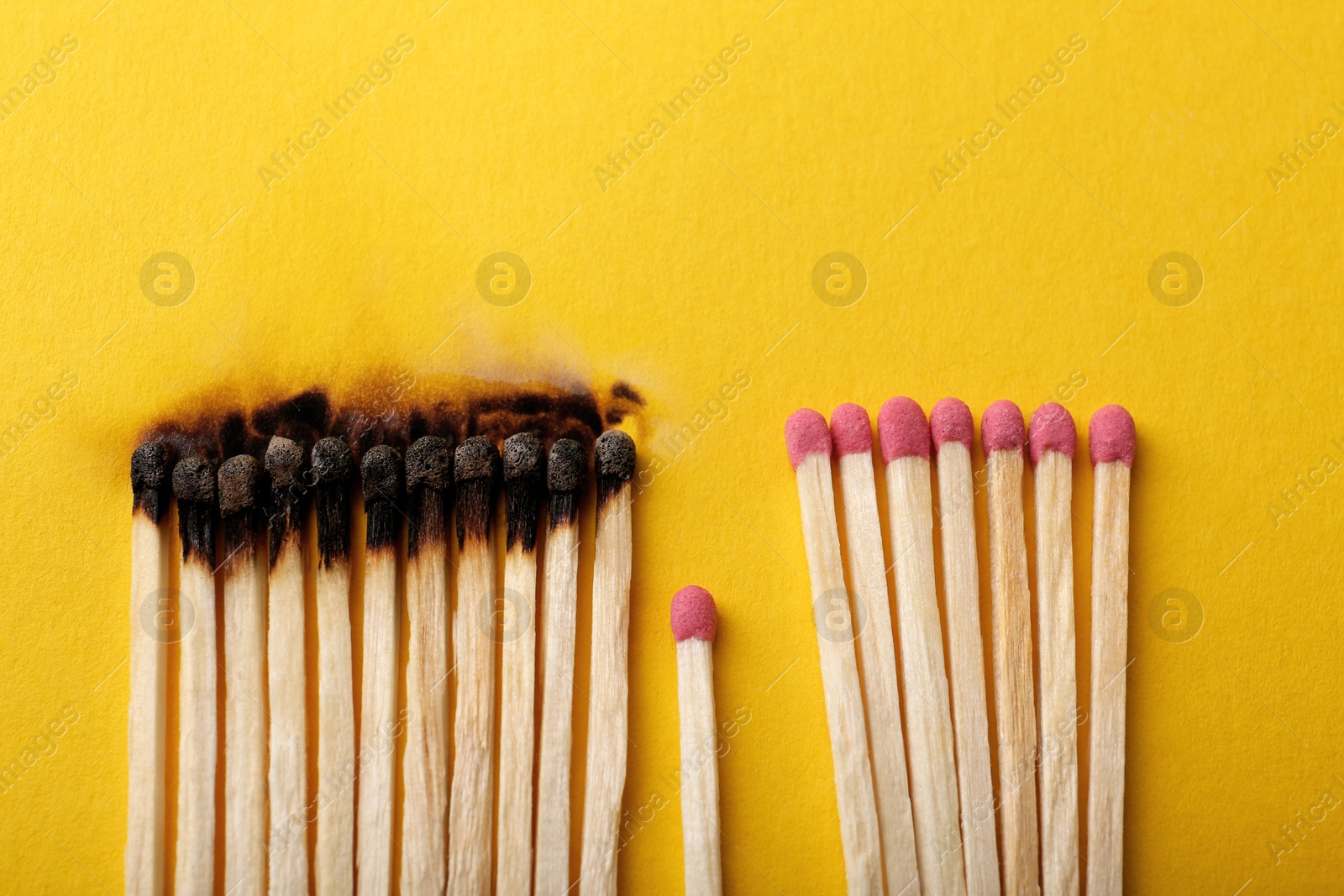 Photo of Burnt and whole matches on yellow background, flat lay