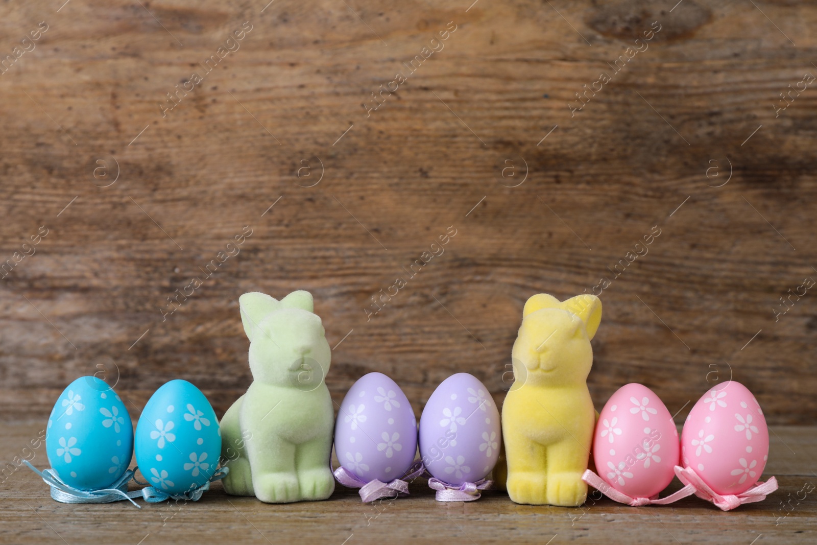 Photo of Easter bunnies and painted eggs on wooden background, space for text