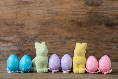 Photo of Easter bunnies and painted eggs on wooden background, space for text