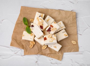 Photo of Pieces of delicious nutty nougat on white textured table, top view