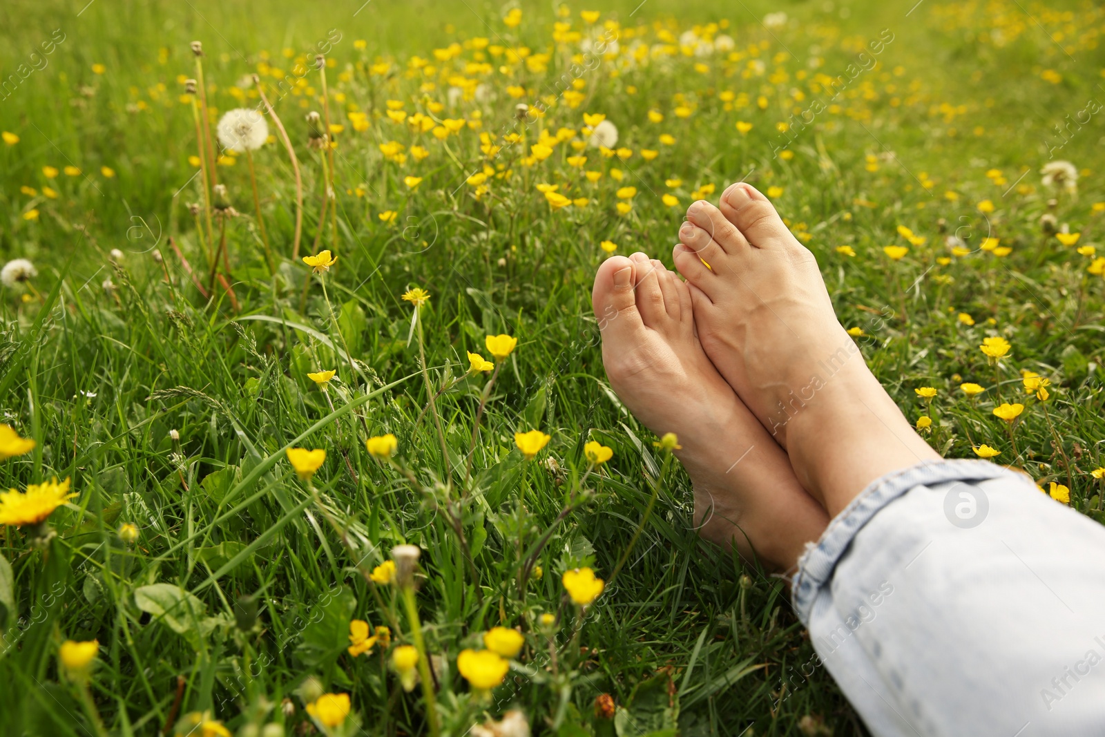 Photo of Woman sitting barefoot on green grass outdoors, closeup. Space for text