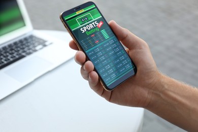 Man betting on sports using smartphone at table, closeup. Bookmaker website on display