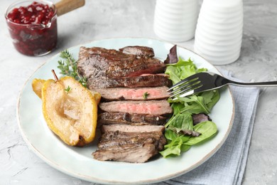 Photo of Delicious roasted beef meat, caramelized pear and greens served on light table, closeup