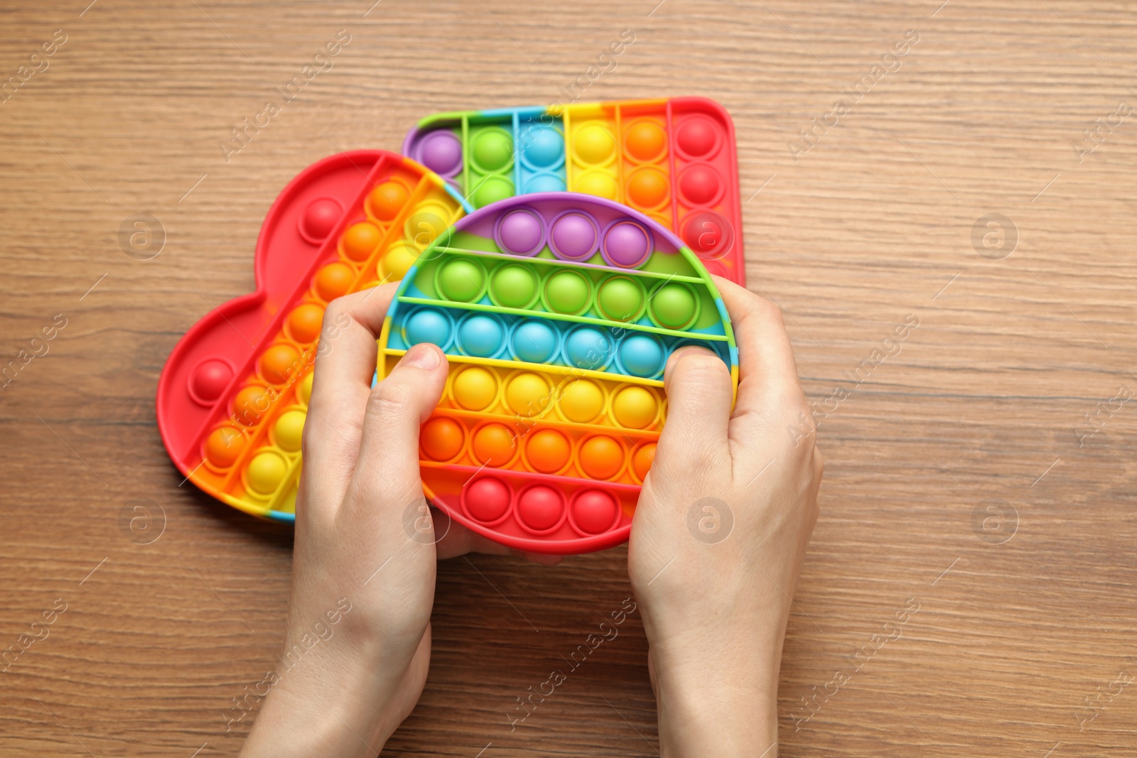 Photo of Woman using pop it fidget toy at wooden table, top view