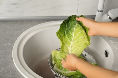 Photo of Woman washing leaf of savoy cabbage under tap water in kitchen sink, closeup