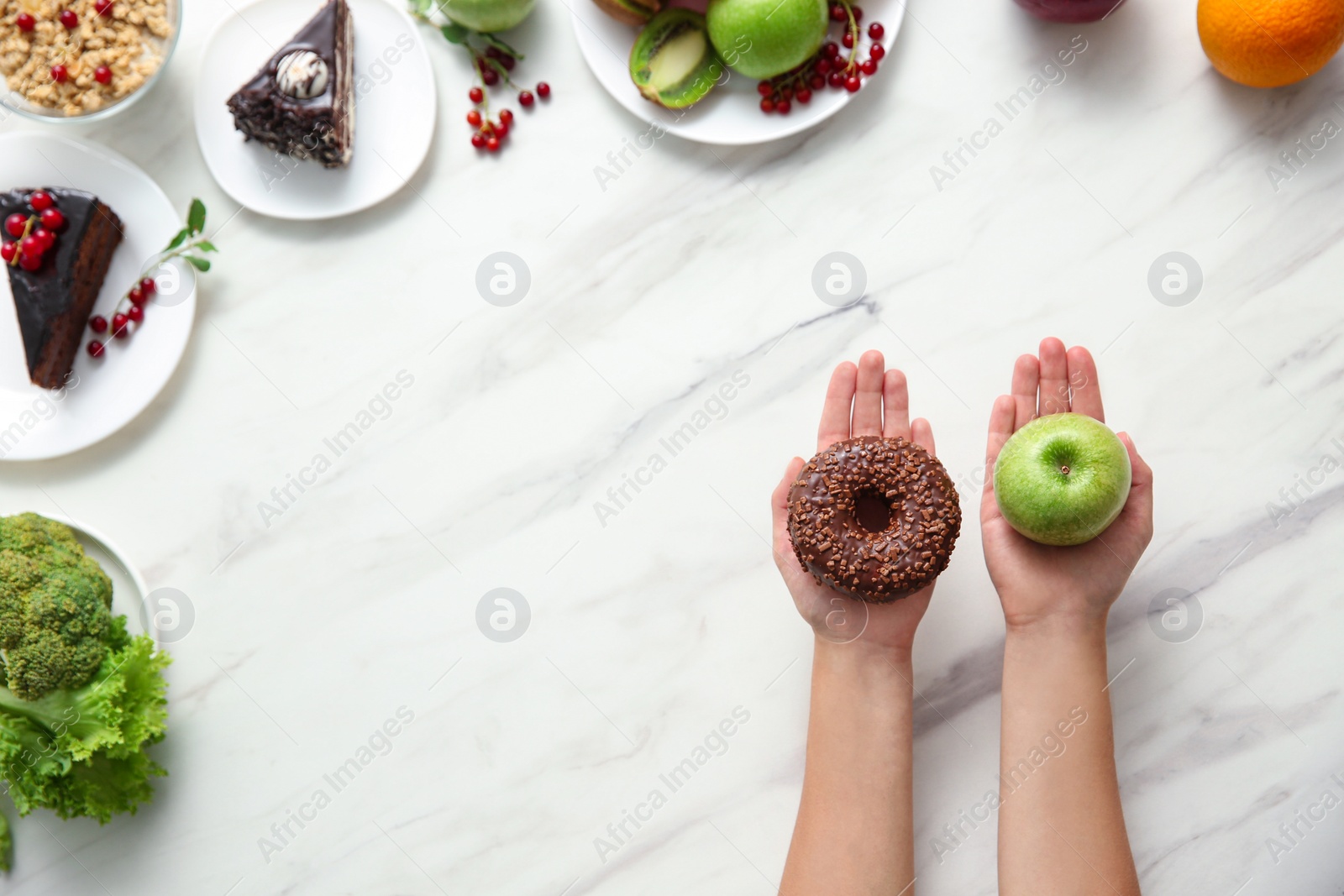 Photo of Top view of woman choosing between sweets and healthy food on white marble table, space for text