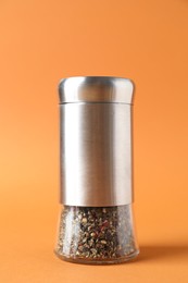 Photo of One shaker with mix of peppers on orange background