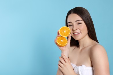 Photo of Woman holding juicy cut orange on light blue background, space for text. Spa treatment