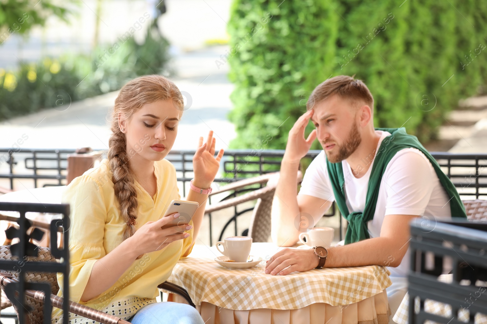 Photo of Young couple arguing while sitting in cafe, outdoors. Problems in relationship