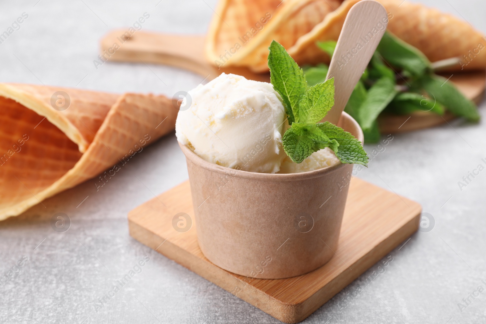 Photo of Delicious vanilla ice cream with mint in paper cup on light grey table, closeup