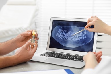 Photo of Doctor showing patient X-ray picture and educational model of dental implant in clinic, closeup