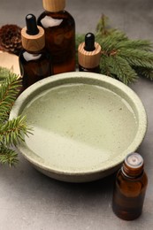 Photo of Bowl of essential oil and fir twigs on grey table. Aromatherapy treatment