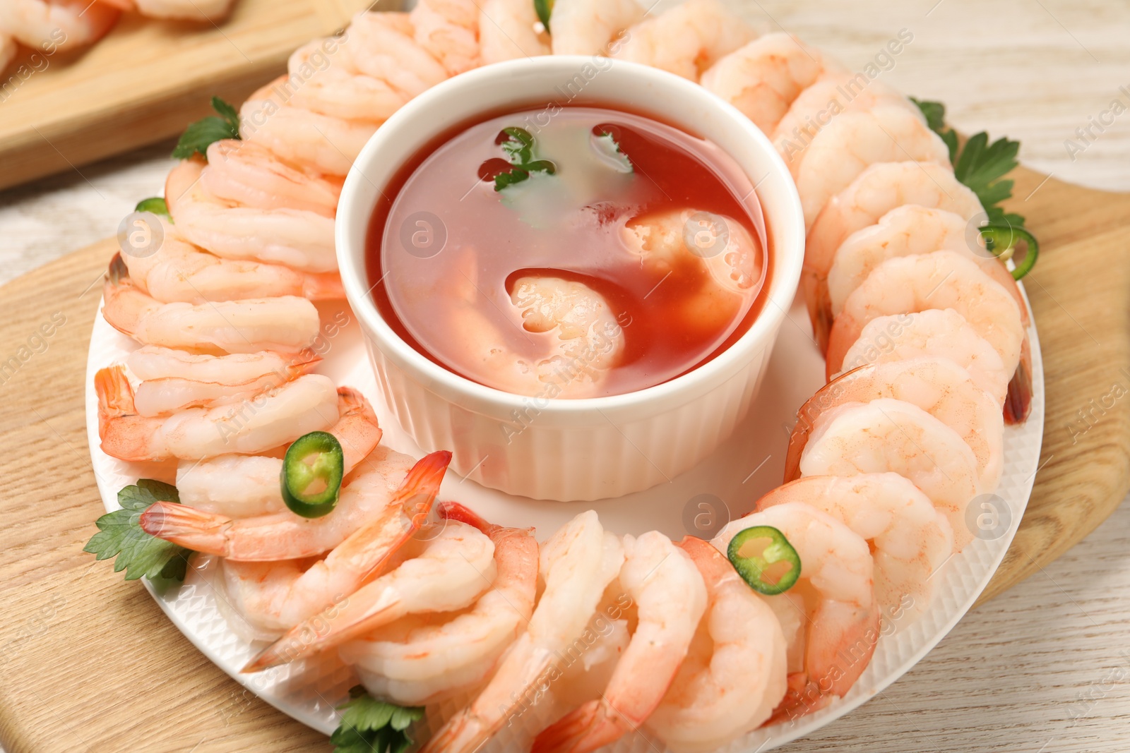 Photo of Tasty boiled shrimps with cocktail sauce, chili and parsley on light wooden table, closeup