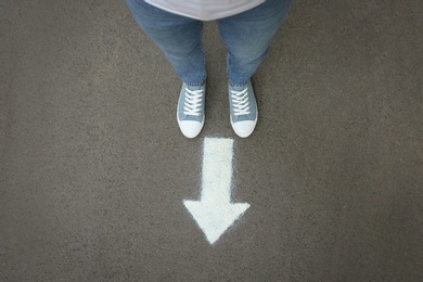 Photo of Woman standing near arrow on asphalt, top view