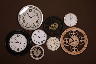 Photo of Collection of stylish clocks on brown wall