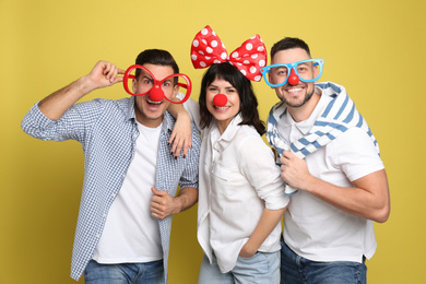 Group of friends with funny accessories on yellow background. April fool's day