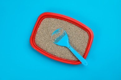 Photo of Cat litter tray with filler and scoop on light blue background, top view
