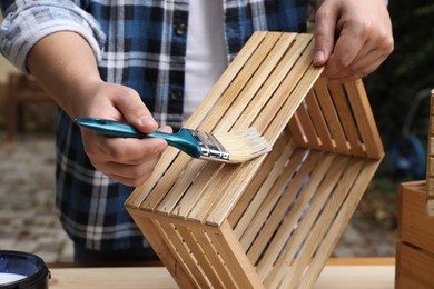 Photo of Man applying varnish onto wooden crate at table outdoors, closeup