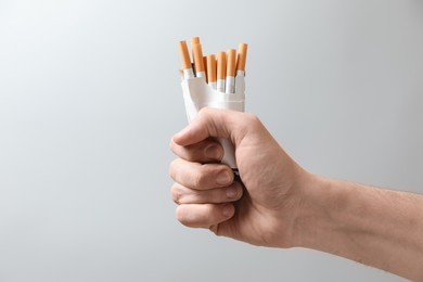Photo of Stop smoking. Man holding pack with cigarettes on grey background, closeup