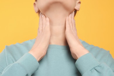 Woman suffering from sore throat on orange background, closeup