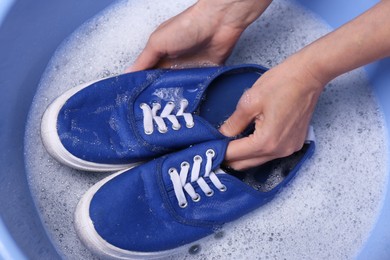 Photo of Woman washing sport shoes in plastic basin, top view