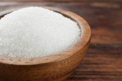 Photo of Granulated sugar in bowl on wooden table, closeup