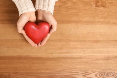 Photo of Woman holding decorative heart on wooden background, top view with space for text
