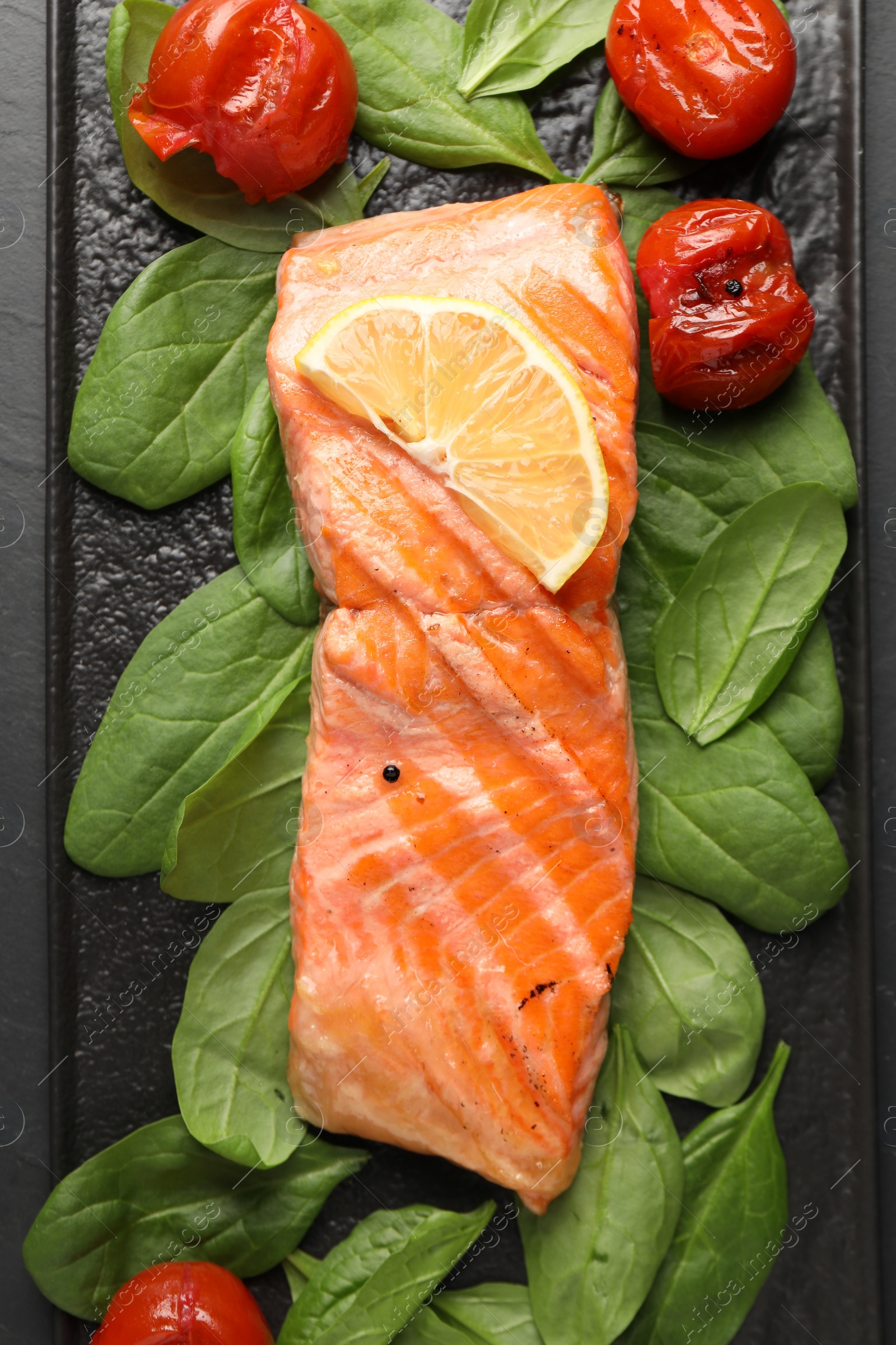 Photo of Tasty grilled salmon with tomatoes, spinach and lemon on table, top view