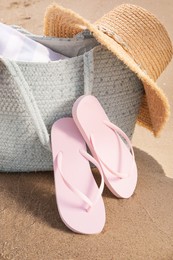 Photo of Bag with beach accessories and flip flops on sand
