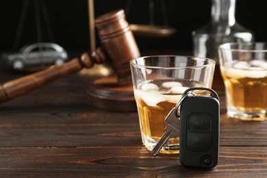 Photo of Car key, glass of alcohol near gavel on wooden table, space for text. Dangerous drinking and driving