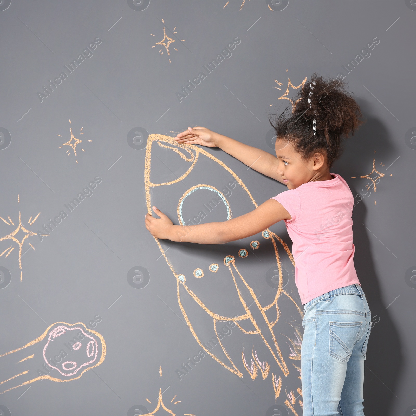 Photo of African-American child playing with chalk rocket drawing on grey background