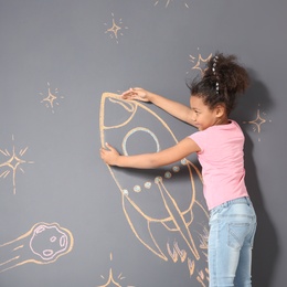 Photo of African-American child playing with chalk rocket drawing on grey background